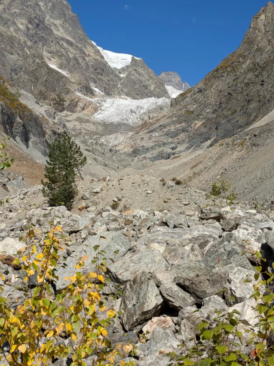 Berglandschaft mit Gletscher, Herbstblättern und Sträuchern, umgeben von Felsbrocken.
